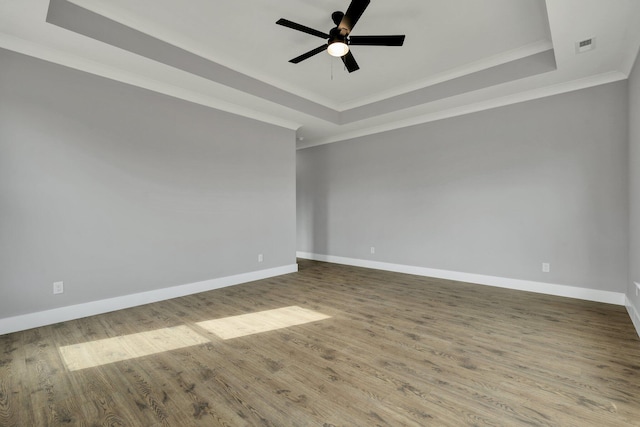 spare room with a tray ceiling, crown molding, dark wood-type flooring, ceiling fan, and baseboards