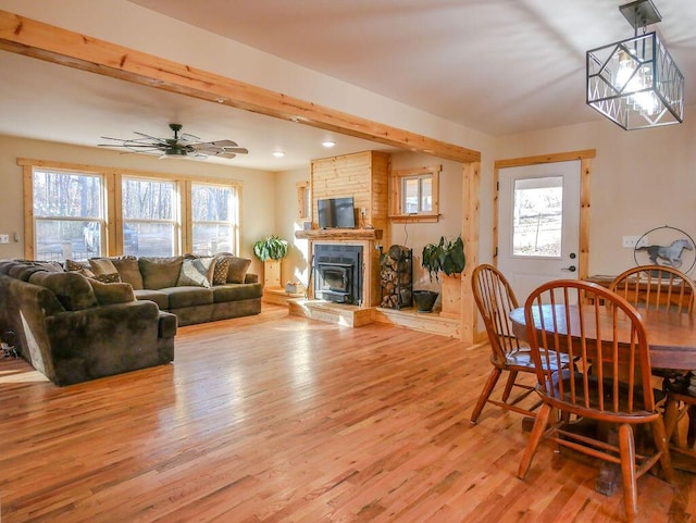 dining area featuring light wood-type flooring, a stone fireplace, ceiling fan, and a healthy amount of sunlight