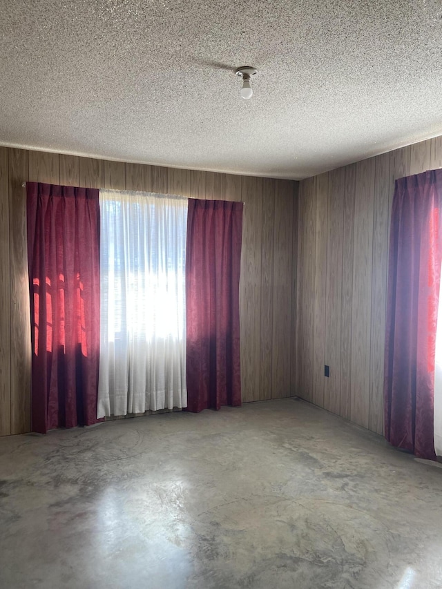 empty room with wood walls, concrete flooring, and a textured ceiling