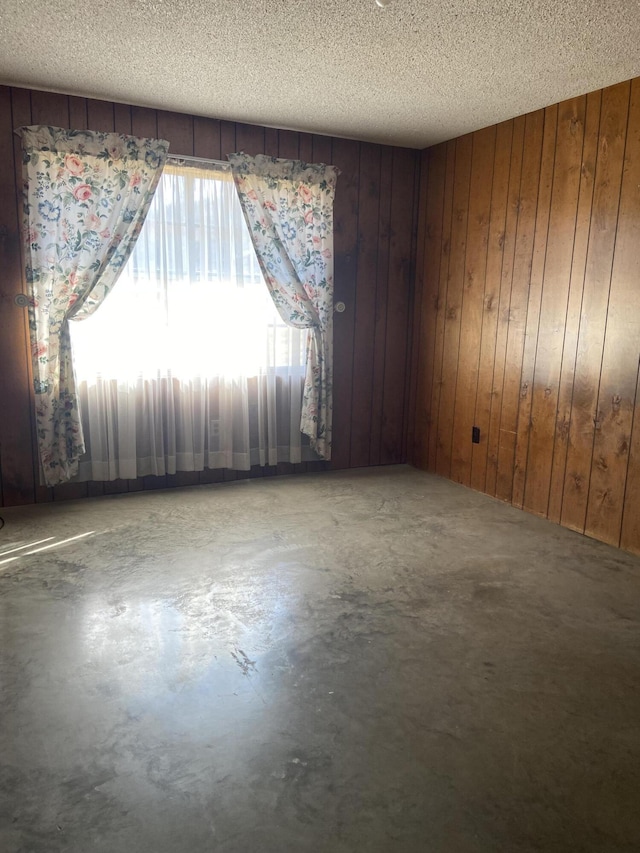 spare room with wood walls, concrete flooring, and a textured ceiling