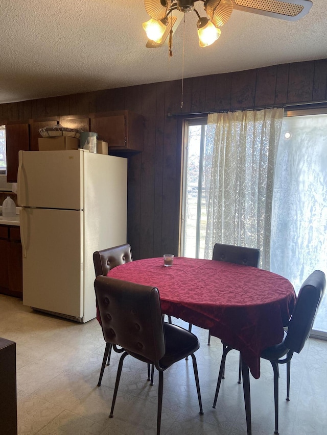 dining room featuring ceiling fan, wood walls, and a textured ceiling