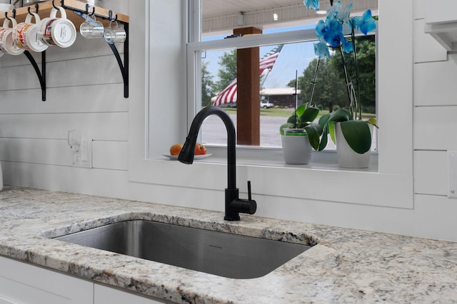 interior details featuring white cabinetry, light stone countertops, and sink