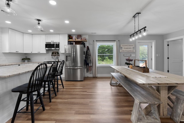 kitchen featuring pendant lighting, white cabinetry, a kitchen breakfast bar, light stone counters, and stainless steel appliances