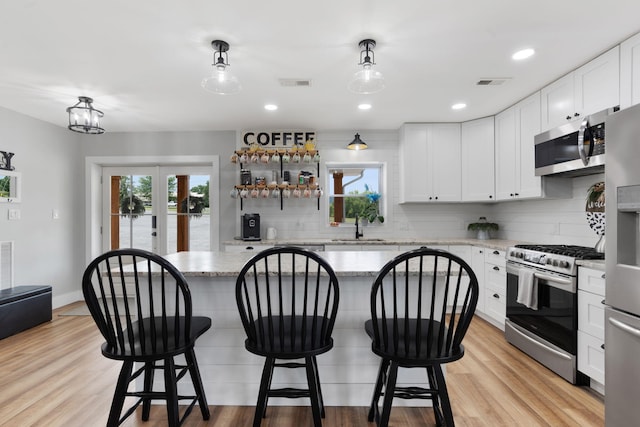 kitchen with decorative light fixtures, sink, white cabinets, light stone counters, and stainless steel appliances