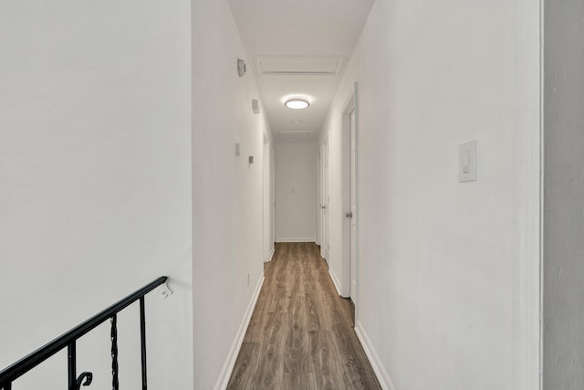 hall with baseboards, attic access, wood finished floors, and an upstairs landing
