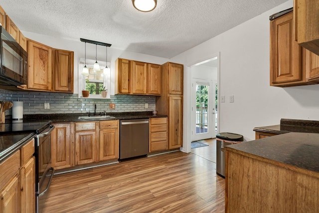 kitchen featuring decorative backsplash, dark countertops, light wood-style floors, a sink, and appliances with stainless steel finishes