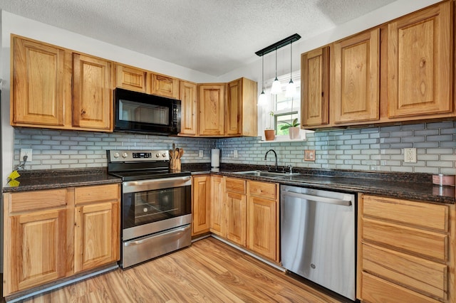 kitchen featuring light wood-style floors, a textured ceiling, a sink, hanging light fixtures, and stainless steel appliances