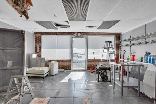 interior space with a drop ceiling and brick wall