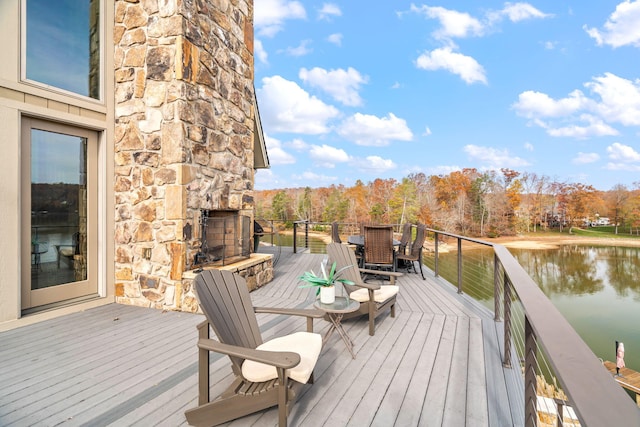 wooden deck with a water view and an outdoor stone fireplace