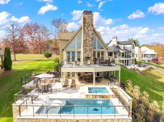 back of house with a balcony, an outdoor stone fireplace, a swimming pool with hot tub, a patio, and a yard