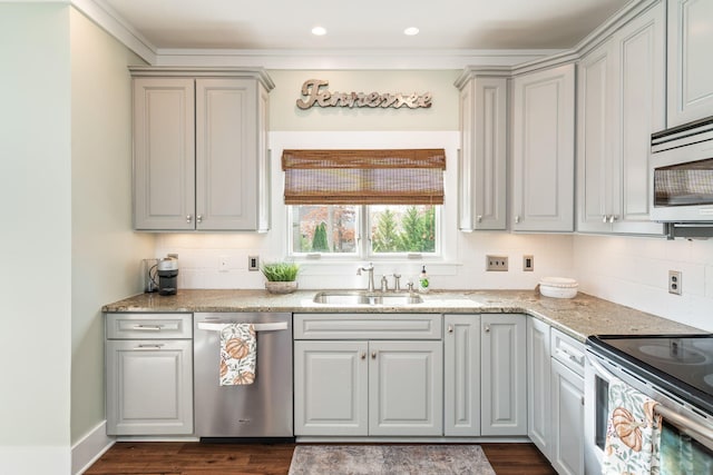 kitchen with stainless steel appliances, dark hardwood / wood-style floors, ornamental molding, light stone counters, and sink