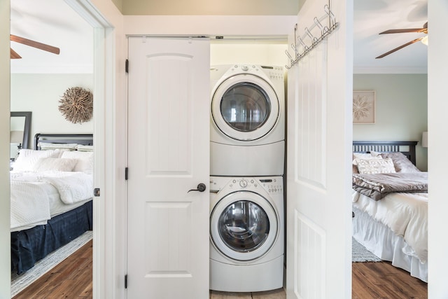 laundry room with ceiling fan, stacked washing maching and dryer, dark wood-type flooring, and crown molding