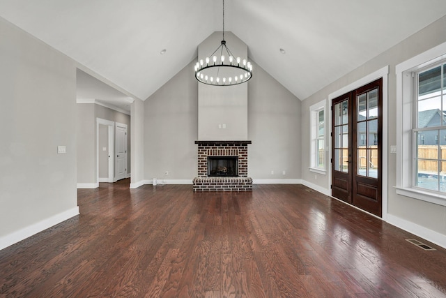 unfurnished living room featuring a chandelier, dark hardwood / wood-style flooring, plenty of natural light, and a brick fireplace