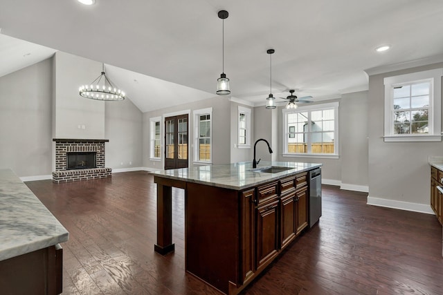 kitchen with a kitchen island with sink, ceiling fan with notable chandelier, sink, decorative light fixtures, and light stone counters