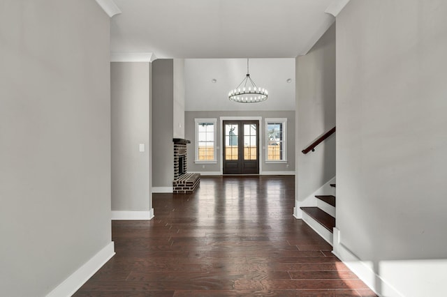 foyer entrance featuring french doors, crown molding, a brick fireplace, dark hardwood / wood-style floors, and a notable chandelier