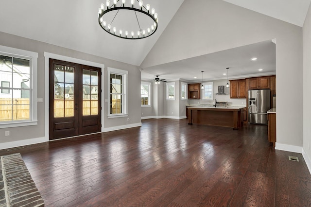 foyer entrance with ceiling fan with notable chandelier, dark wood-type flooring, high vaulted ceiling, and french doors