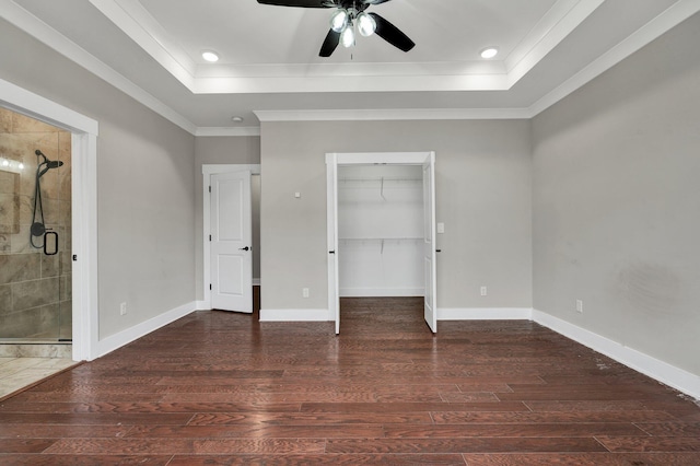 unfurnished bedroom with a tray ceiling, ensuite bath, ceiling fan, and dark wood-type flooring