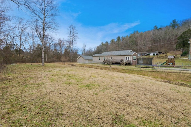 view of yard featuring a playground, a wooden deck, and a trampoline