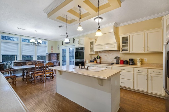 kitchen with pendant lighting, dark hardwood / wood-style floors, black double oven, a center island with sink, and custom exhaust hood