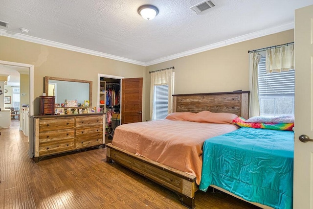 bedroom with a walk in closet, wood-type flooring, ornamental molding, and a textured ceiling