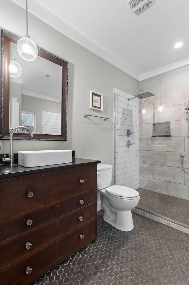 bathroom featuring toilet, ornamental molding, a tile shower, and vanity