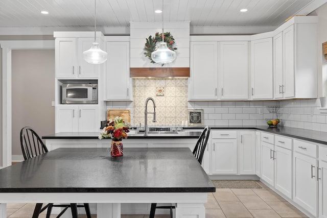 kitchen featuring decorative light fixtures, backsplash, built in microwave, a breakfast bar area, and white cabinets