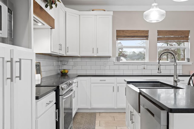 kitchen featuring white cabinets, wall chimney range hood, stainless steel appliances, decorative backsplash, and hanging light fixtures