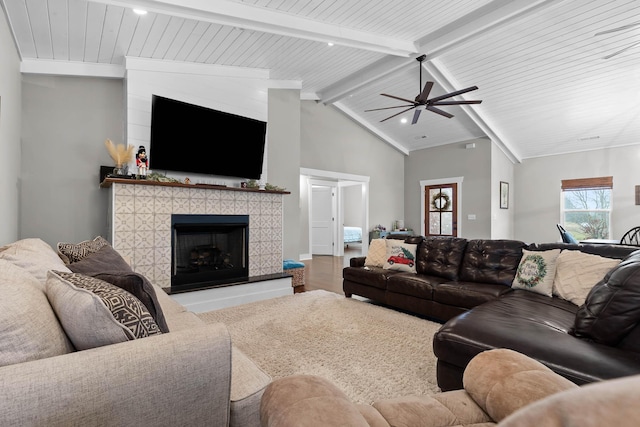 living room with ceiling fan, a tile fireplace, and vaulted ceiling with beams