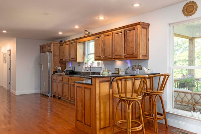 kitchen featuring a kitchen breakfast bar, stainless steel refrigerator, dark hardwood / wood-style flooring, and kitchen peninsula