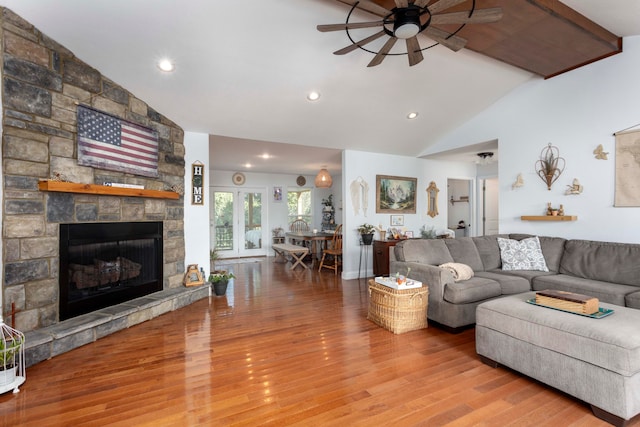 living room featuring a stone fireplace, ceiling fan, hardwood / wood-style floors, and high vaulted ceiling