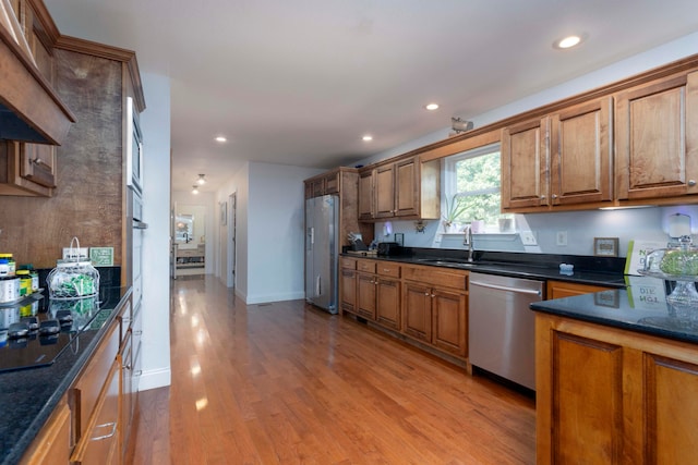 kitchen with stainless steel appliances, light hardwood / wood-style flooring, dark stone counters, and sink