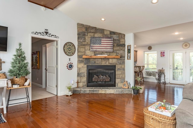 living room with a stone fireplace, wood-type flooring, and vaulted ceiling