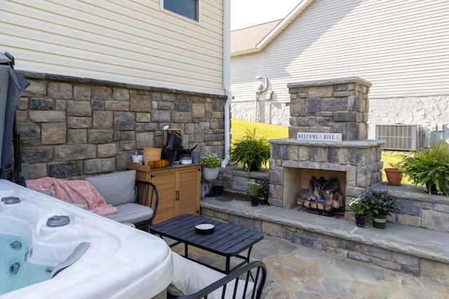 view of patio featuring an outdoor stone fireplace, a hot tub, and central air condition unit