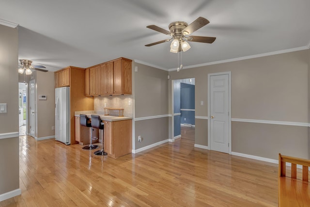 kitchen featuring ornamental molding, a breakfast bar, ceiling fan, white refrigerator, and light hardwood / wood-style flooring