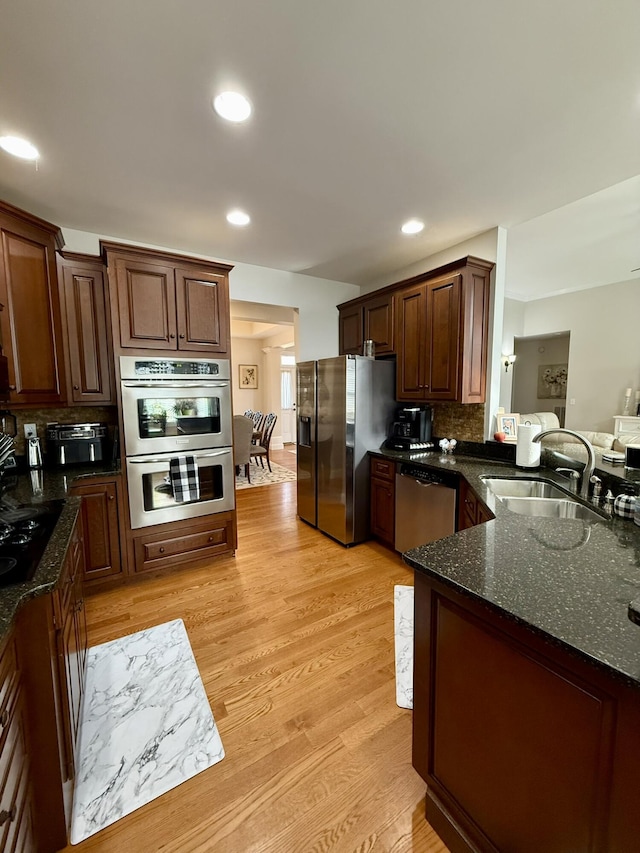 kitchen featuring appliances with stainless steel finishes, sink, backsplash, dark stone counters, and light hardwood / wood-style floors