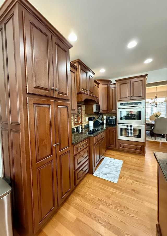 kitchen with dark stone countertops, stainless steel double oven, and light wood-type flooring