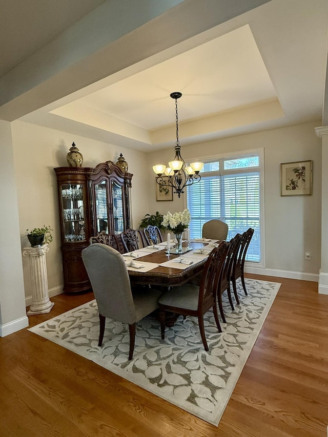 dining room with a tray ceiling, a chandelier, and hardwood / wood-style flooring