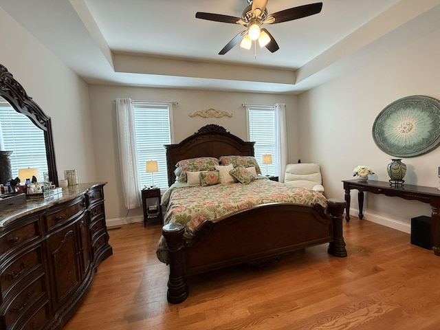 bedroom featuring ceiling fan, light hardwood / wood-style floors, and a tray ceiling