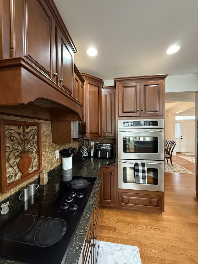 kitchen featuring backsplash, appliances with stainless steel finishes, light hardwood / wood-style floors, and dark stone countertops