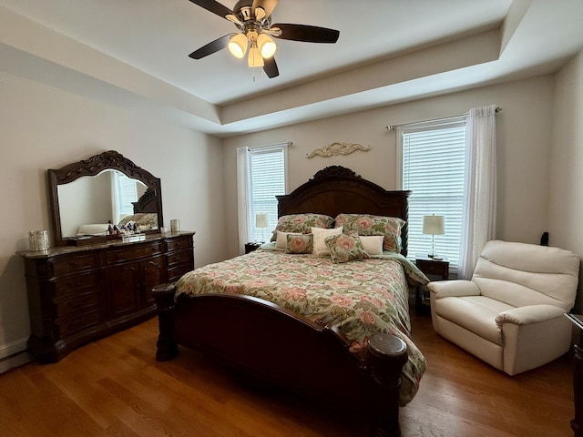 bedroom with a raised ceiling, hardwood / wood-style floors, and ceiling fan