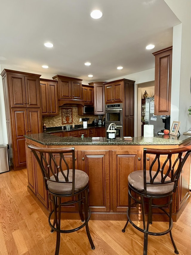 kitchen with backsplash, a kitchen bar, kitchen peninsula, stainless steel double oven, and light wood-type flooring