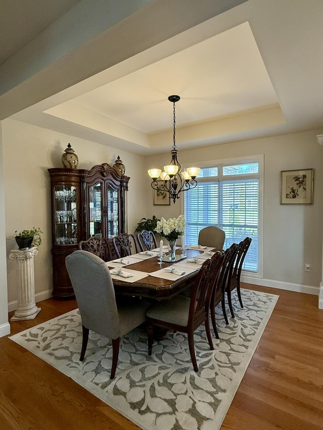 dining area featuring hardwood / wood-style floors, a notable chandelier, and a raised ceiling