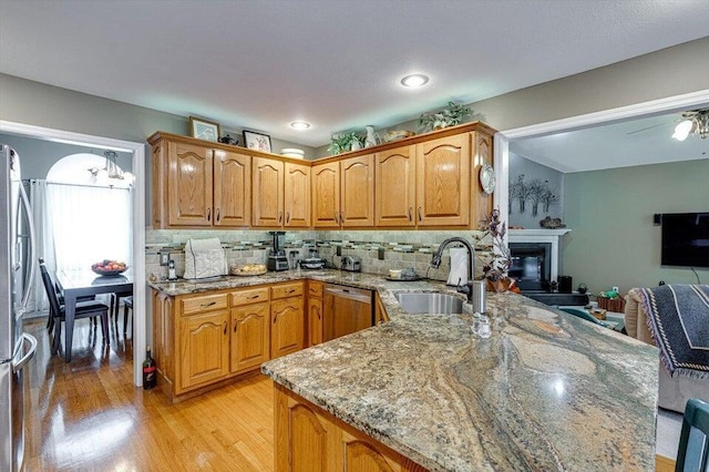 kitchen featuring kitchen peninsula, light wood-type flooring, tasteful backsplash, stainless steel appliances, and sink