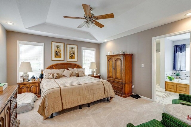 bedroom with a raised ceiling, ensuite bath, ceiling fan, and light carpet