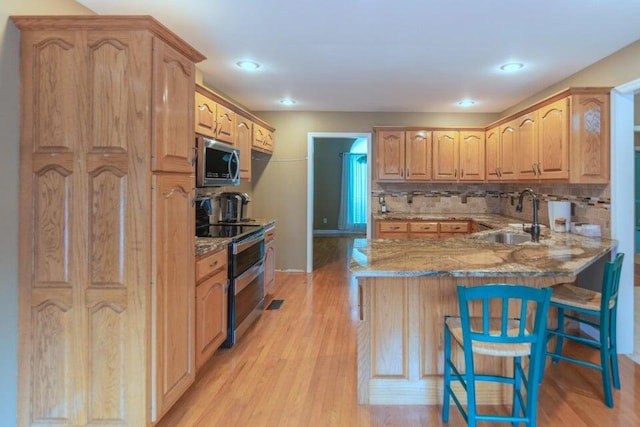 kitchen with sink, a breakfast bar area, light hardwood / wood-style floors, kitchen peninsula, and stainless steel appliances