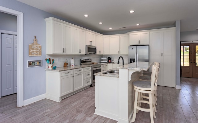 kitchen featuring light stone countertops, appliances with stainless steel finishes, a kitchen island with sink, light hardwood / wood-style floors, and white cabinetry