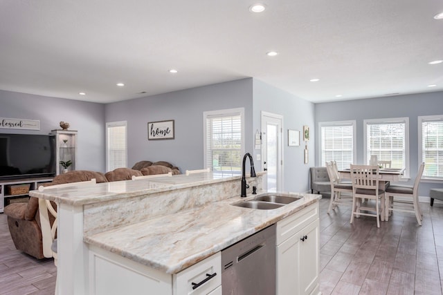 kitchen featuring dishwasher, sink, a kitchen island with sink, white cabinets, and light wood-type flooring