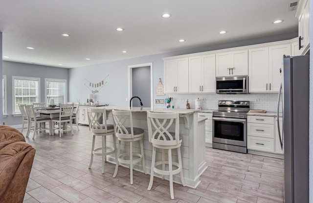 kitchen with a kitchen island with sink, light wood-type flooring, a kitchen bar, white cabinetry, and stainless steel appliances