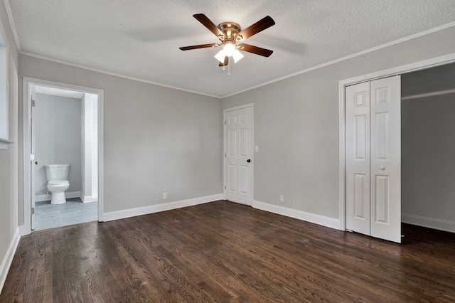 unfurnished bedroom featuring ceiling fan, dark wood-type flooring, ensuite bathroom, a textured ceiling, and a closet