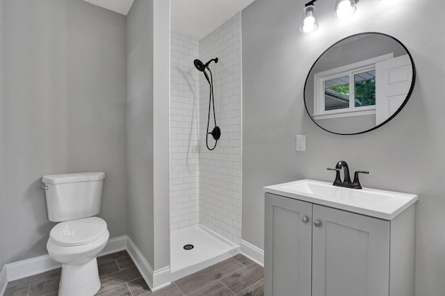 bathroom with vanity, toilet, a textured ceiling, and a tile shower